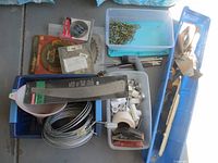 Blue plastic bins containing assorted tools, coiled wire, pipe fittings, screws, and hand tools with wooden handles