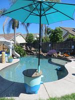 Outdoor photo showing the side table/umbrella stand with turquoise umbrella set up by a backyard pool.