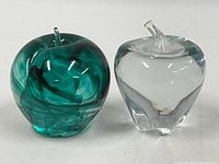 Front view of the green swirl glass peach and clear glass apple side by side on a white background showing shape, color, and glossy finish.