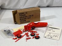 Red plastic racing car model parts including body shell, wheels, and chassis components laid out next to original box and motor.