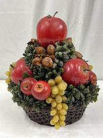 Front view of the faux fruit basket showing red apples, yellow grapes, pecans, green leaves, and the woven basket base with the bug on top.