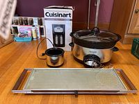 Lot contents showing Cuisinart coffeemaker and box, Crockpot slow cooker, Little Dipper warmer, and Salton hot tray on wooden floor.