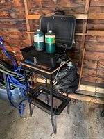 Full view of portable propane BBQ on metal and wood stand with two propane bottles on grill and BBQ cover attached.
