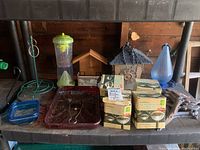Photo showing multiple bird feeders, iron lawn spikes with circular bases, boxed solar garden lights, and a blue water scoop arranged on a shelf.