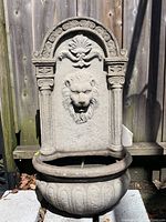 Front view of the stone style wall mount water fountain with lion head design and basin.