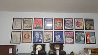 Full view of 16 framed sheet music covers arranged on wall above mantel with clocks