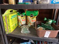 Wide view showing two Miracle-Gro Shake 'n Feed bags, PearExceed bag, spray head, and brown bin with garden tools on black shelf.