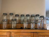 Front overview of 14 vintage canning jars arranged on wooden surface, showing variety of sizes with metal lids and embossed glass.