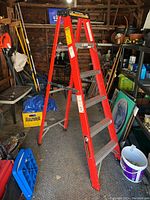 Full view of the red fiberglass and aluminum step ladder standing open in a workshop environment, showing overall condition and structure.