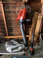 Full view of Black & Decker leaf blower/mulcher with long tube attached and leaf collection bag on table below.