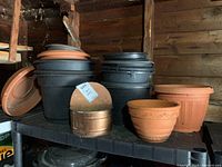 Black plastic pots stacked, with terracotta and metal planter front left on shelving unit.