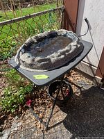 Small electric pond filled with water, stone-textured oval shape on black folding table outdoors with chain link fence background.