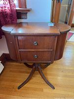 Front view of vintage wooden sewing cabinet with drawers and closed side compartments showing scratches and stains on top.