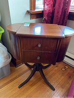 Front view of vintage wood sewing cabinet showing rounded side panels and two drawers with decorative handles.