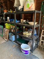 Two black plastic shelving units with various items placed on shelves in a garage setting, showing the structure and condition of the shelves.
