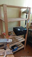 Full view of wooden shelving unit showing three shelves, light wood tone, and slatted shelf design. Various items visible on lower shelves but not included in sale.
