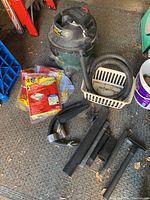 Full view of Shop-Vac and assorted attachments laid out on floor including vacuum hose, plastic basket, crevice tools, and packaged dust bags.