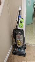 Side view of the Bissell vacuum standing upright against a wall, showing the main vacuum unit, handle, and attached cleaning accessories.