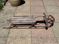 Side view of vintage Spartan sled showing wooden slats and red metal frame on paved surface.