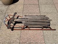 Side view of vintage Spartan sled lying on pavement, showing wooden slats and metal frame