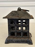 Front view of square blackened metal Chinese case iron lantern with lattice windows and hanging ring on top.