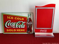 Photo showing the Coca Cola metal sign and the red tabletop bar stand together.