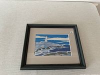 Framed print depicting a lighthouse on rocky shore with ocean waves under a blue sky