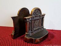 Side-angle photo of one of the antique metal bookends showing its ornate classical relief design and smooth side profile.