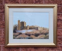 Full view of the watercolor painting framed and hung on a brick wall, showing a castle with detailed structure and natural surroundings under a blue sky.