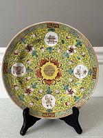 Top view of the round antique Chinese porcelain plate showing the yellow background with five circular medallions containing Chinese characters and surrounding bats and floral motifs.