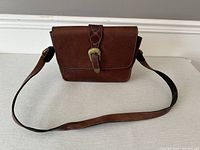 Front view of vintage brown leather crossbody bag with flap and buckle closure. Adjustable shoulder strap attached.