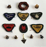 Top-down view of assorted embroidered Boy Scout badges and small leather neckerchief slide arranged on a white background.