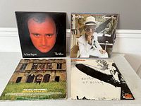 Four vinyl album covers arranged on floor: Phil Collins No Jacket Required, Elton John Greatest Hits, The Rolling Stones 50th Anniversary Collection, Led Zeppelin Touch of Holly.