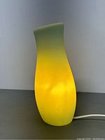 Side view of Mylonit glass lamp showing green to yellow gradient color and curved form lit emitting warm light.