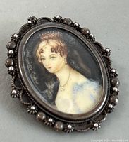 Close-up of oval brooch pendant featuring a watercolour portrait of a woman with decorative silver frame.