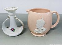 Photo of Bing & Grondahl porcelain candlestick and Johnson Bros pink ceramic pitcher from front angle showing embossed portrait and floral decoration