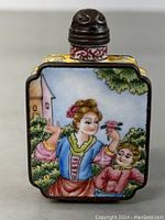 Front view of the square enamel snuff bottle depicting a woman and child in a garden setting under a tree with a building in background