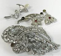 Three assorted costume jewellery brooches shown together: one large rhinestone brooch and two smaller floral brooches with colored accents.