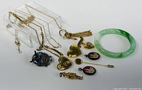 Assorted costume jewelry including necklaces with various pendants such as heart-shaped lockets, owl pendant, stick pin, and jade-like bangle bracelet.