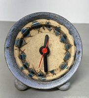 Front view of handmade ceramic clock showing round clock face with blue geometric design and black and red hands.