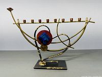 Front view of handmade metal menorah showing overall design, curved arms, and candle holders.