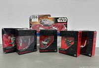 Six Star Wars die-cast vehicles in original packaging, displayed side by side showing front and side views. Packaging is black with red detailing and clear windows displaying the vehicles.