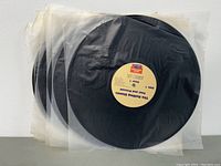 Group of twelve black vinyl records with beige Sonic Workshop labels, each sealed in clear plastic sleeves.
