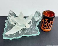 Photo showing the signed frosted glass Inuit art vase on a textured clear glass plate and the reddish-brown etched glass tumbler side by side.