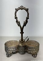 Front view of sterling silver cruet stand with intricate openwork baskets and handle. Two lidded containers with spoons in the center compartments. Shows tarnish.