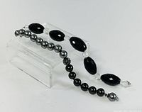 Two bracelets displayed on a clear stand showing bead details and design.