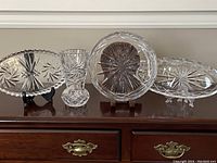 Six vintage Bohemian cut crystal pieces displayed on wooden furniture, includes fruit bowl, celery dish, bud vase, and others
