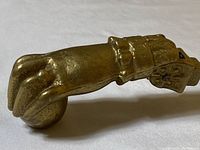 Side view of brass Victorian hand door knocker holding a ball, showing detailed fingers and cuff design.