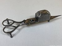 Side view of metal antique candle snuffer with scissor handles and detailed snuffer box showing aged patina.