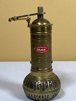 Full view of antique Sozen brass coffee grinder with crank handle and red label on cylinder.